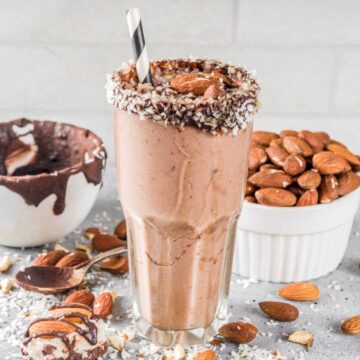 Tall glass filled with a chocolate coconut almond joy smoothie, with the rim dipped in chocolate and coated with shredded coconut.