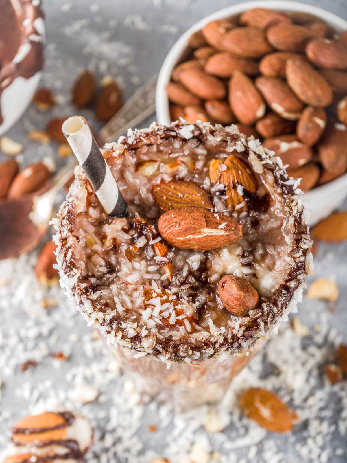 A glass of almond joy smoothie topped with roasted almonds and shredded coconut.