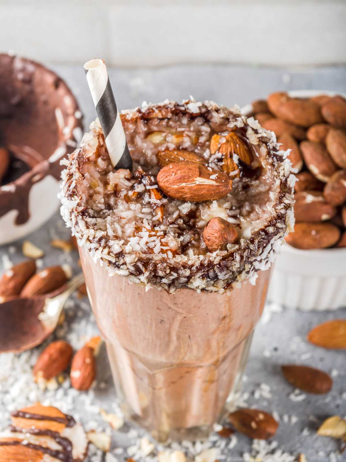 A glass of almond joy smoothie topped with roasted almonds and shredded coconut.