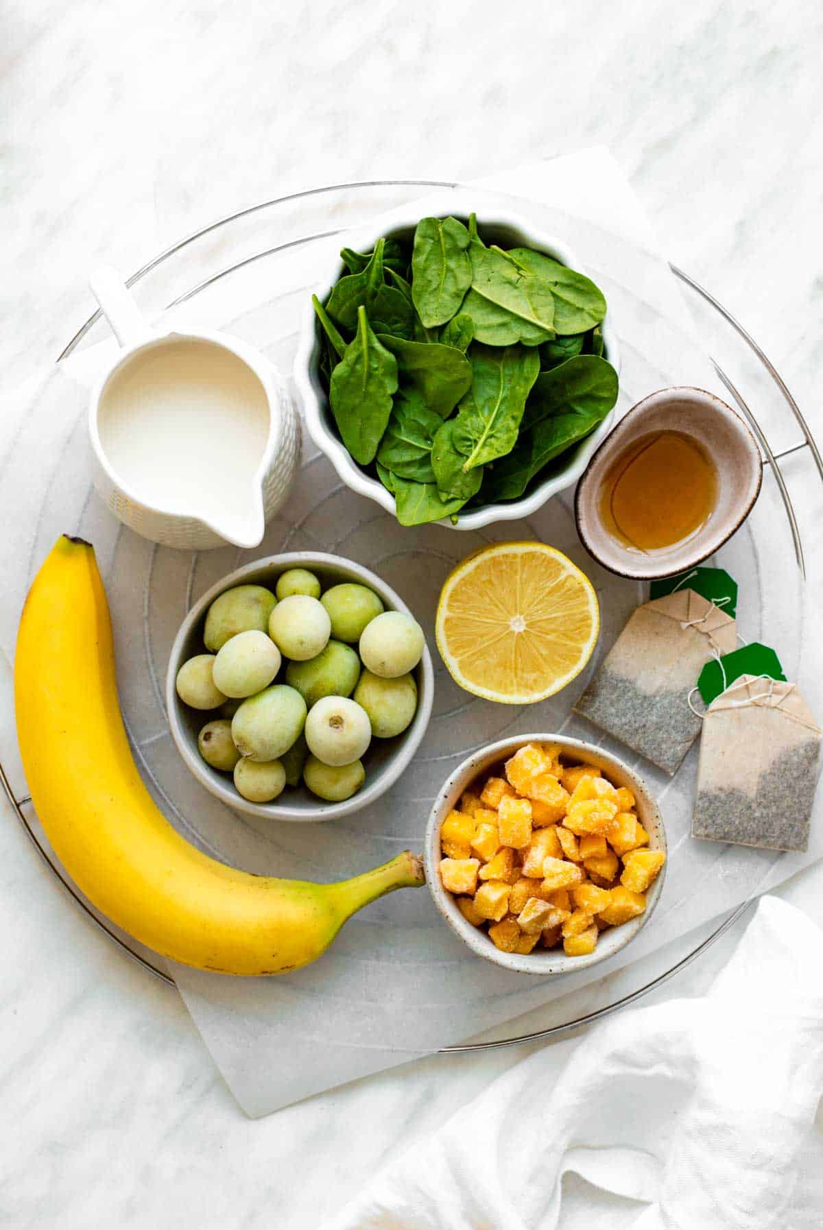 The ingredients needed for this green tea smoothie arranged in various bowls on a tray.