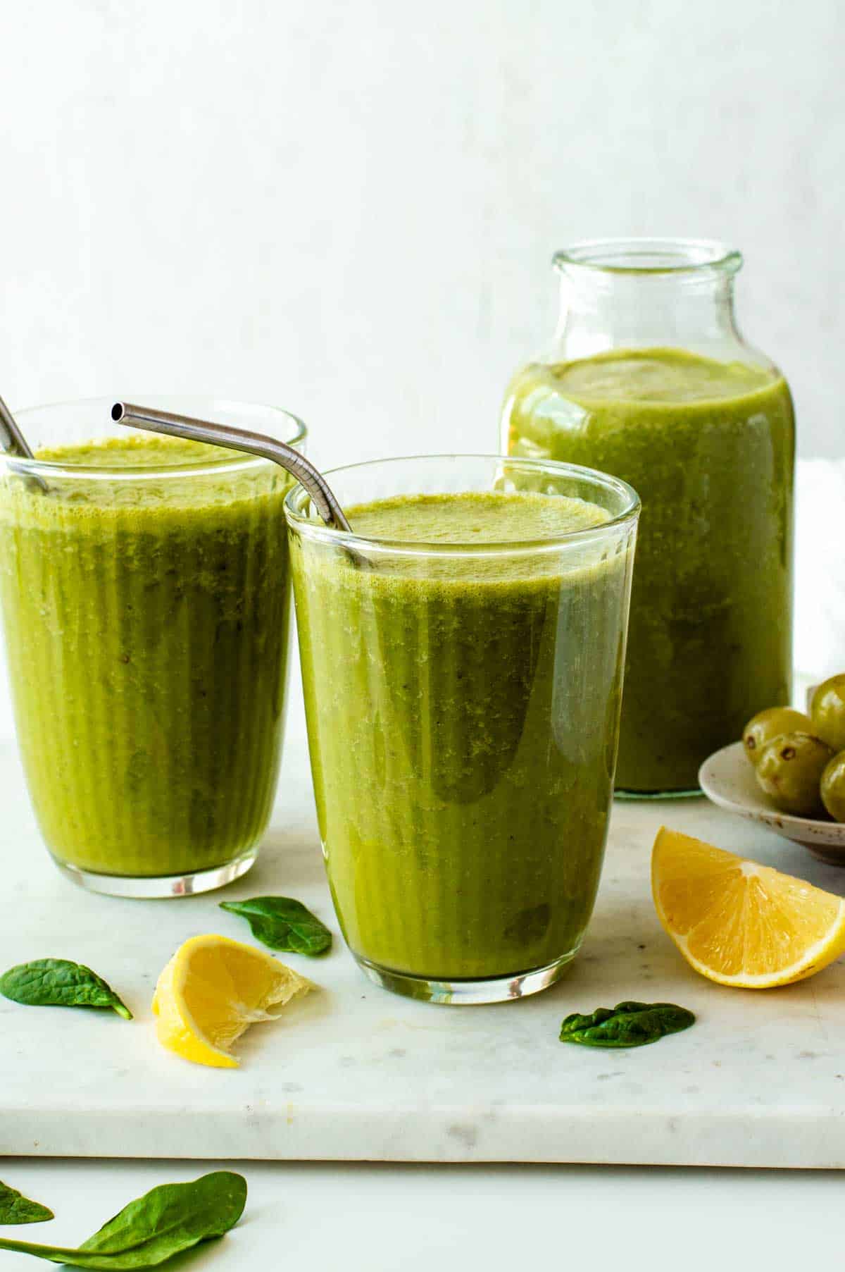 Green tea smoothie in two glasses, served with metal straws.