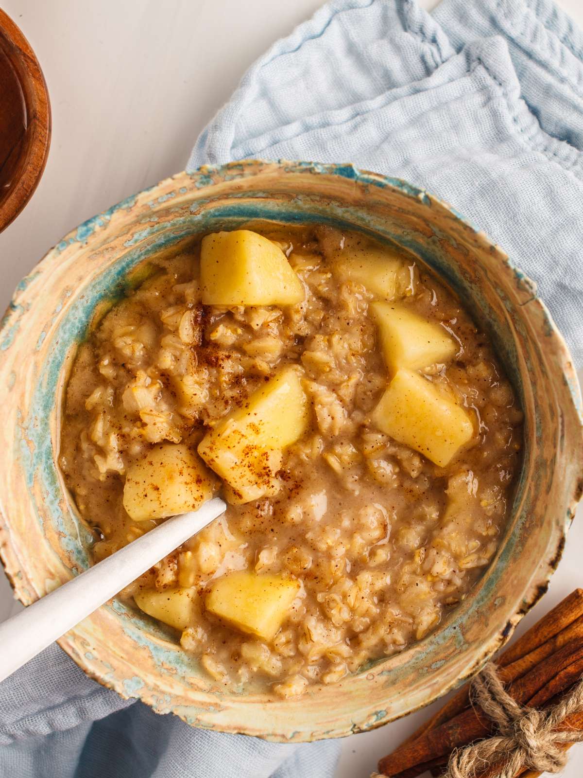 Cinnamon oatmeal in a bowl topped with chopped apple, cinnamon and served with a spoon.