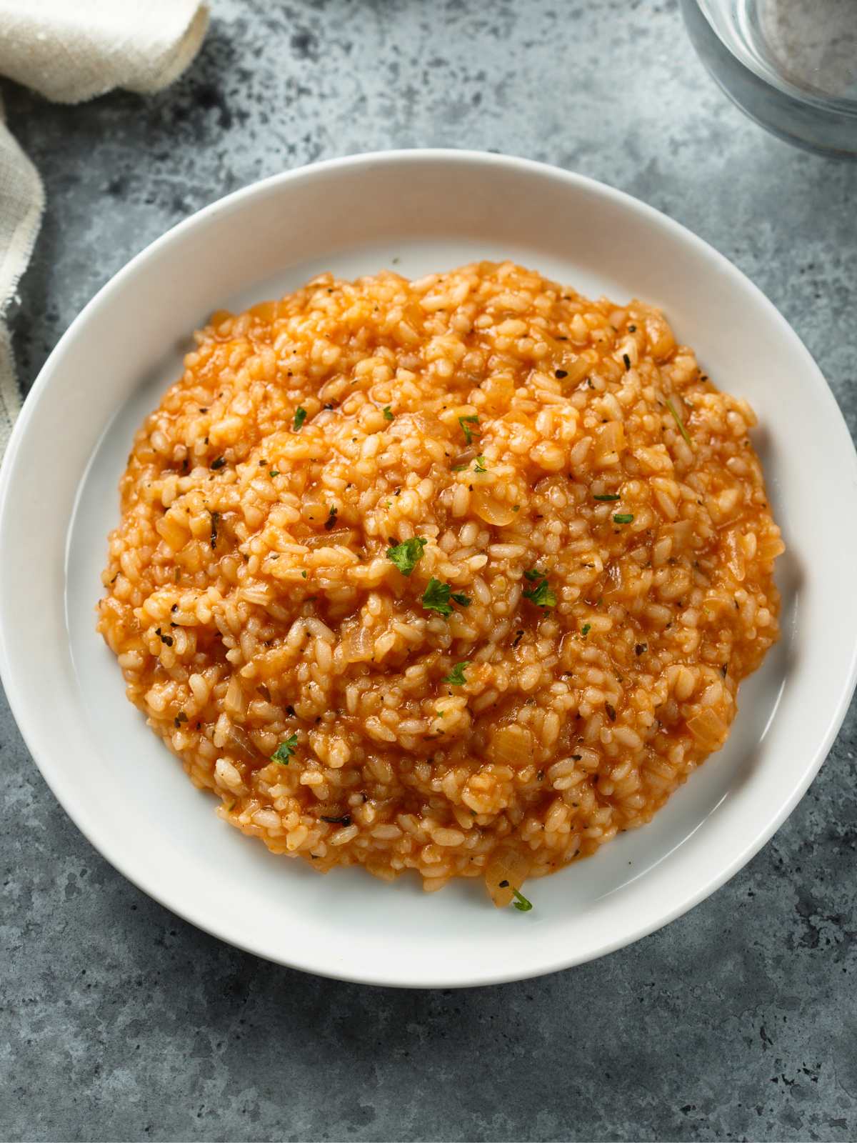 Tomato risotto on a plate topped with fresh herbs.