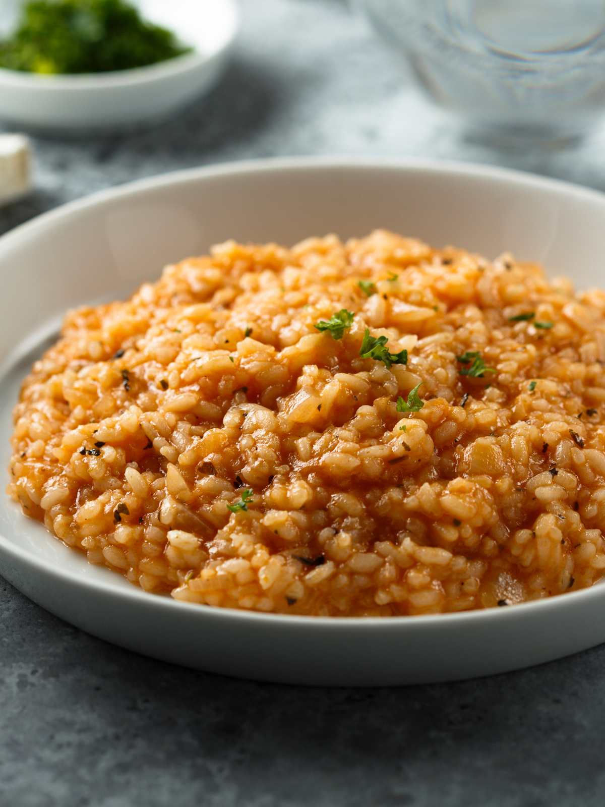 Tomato risotto on a plate topped with chopped herbs.