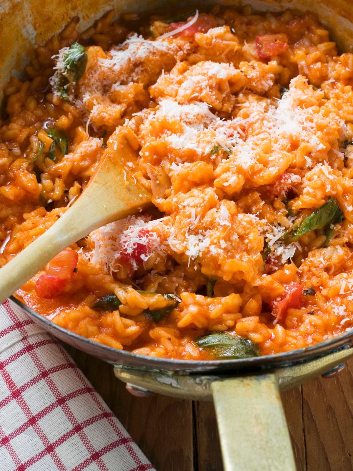 Tomato risotto cooking in a saucepan, topped with vegan parmesan cheese.