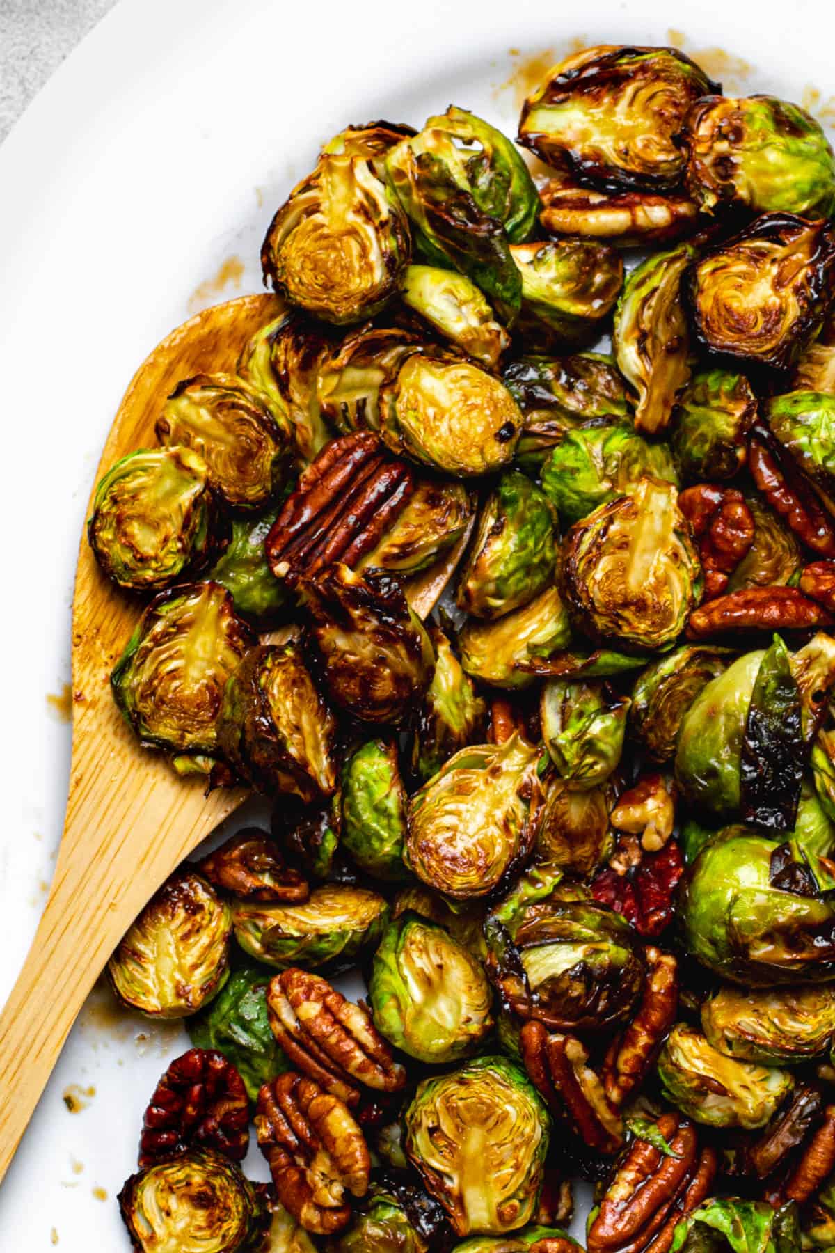 Maple balsamic glazed brussels sprouts on a platter with a wooden serving spoon.