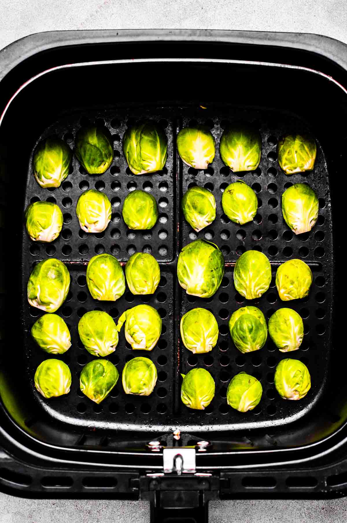 Halved brussels sprouts in an air fryer basket, cut side down.