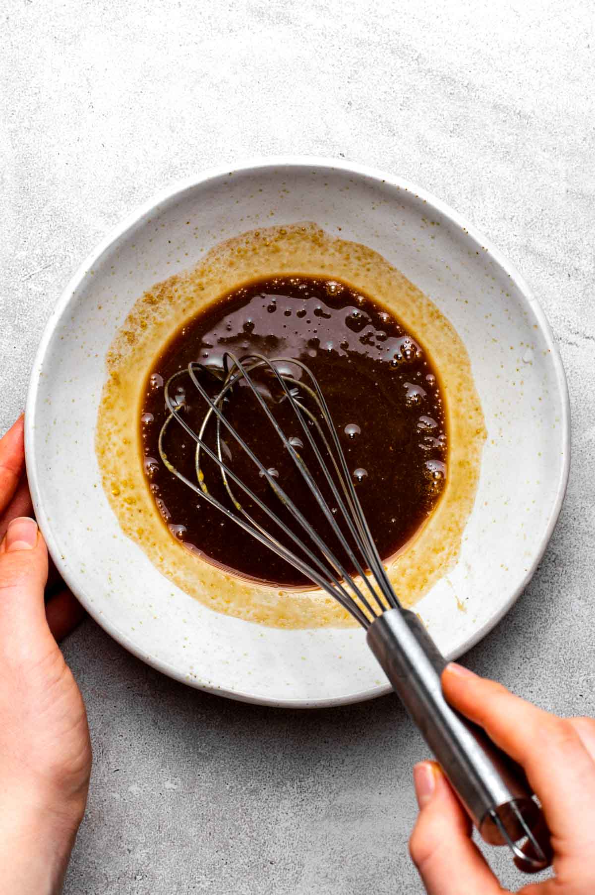 A hand whisking all of the maple glaze ingredients together in a small bowl.
