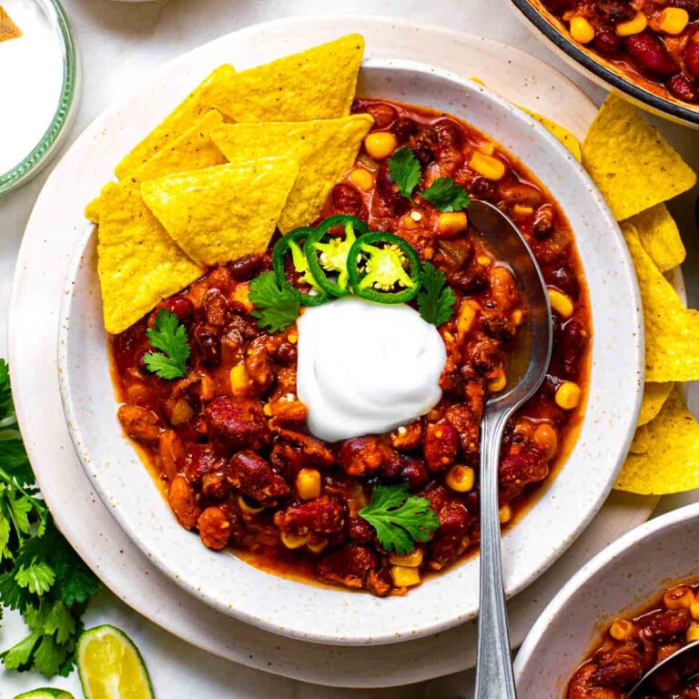 A bowl of three bean chili served with tortilla chips, fresh cilantro, jalapeno slices, and coconut yogurt.