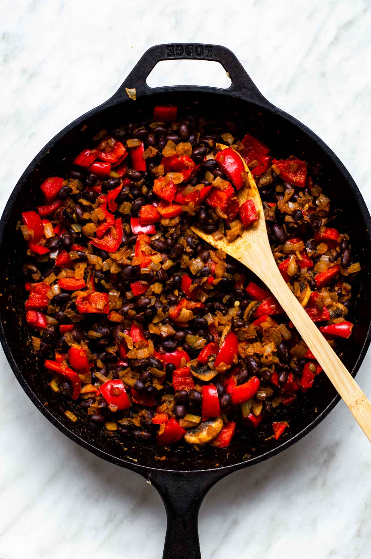 A skillet filled with sauteed vegetables, seasonings, black beans.