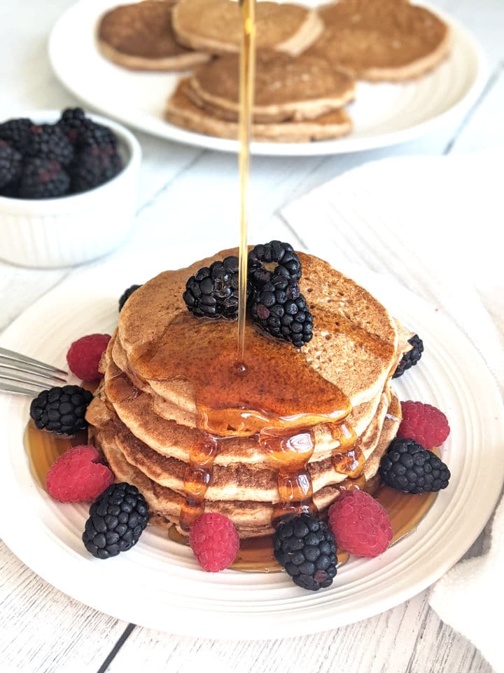 A stack of pancakes on a plate with fresh berries and a drizzle of maple syrup