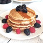 A stack of pancakes on a plate with fresh berries and a drizzle of maple syrup