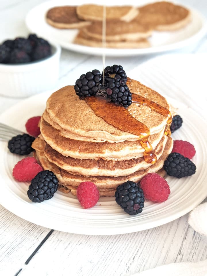 A stack of pancakes on a plate with fresh berries and a drizzle of maple syrup