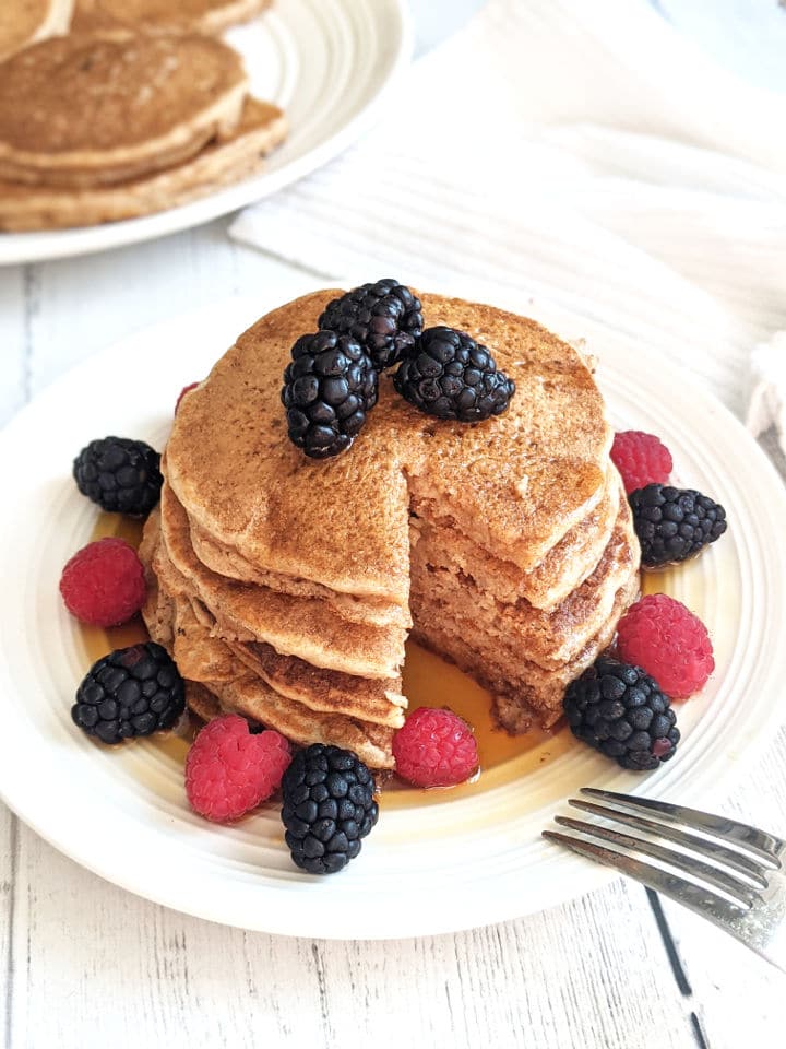 A stack of pancakes on a plate with fresh berries and maple syrup with a slice taken out of the stack.