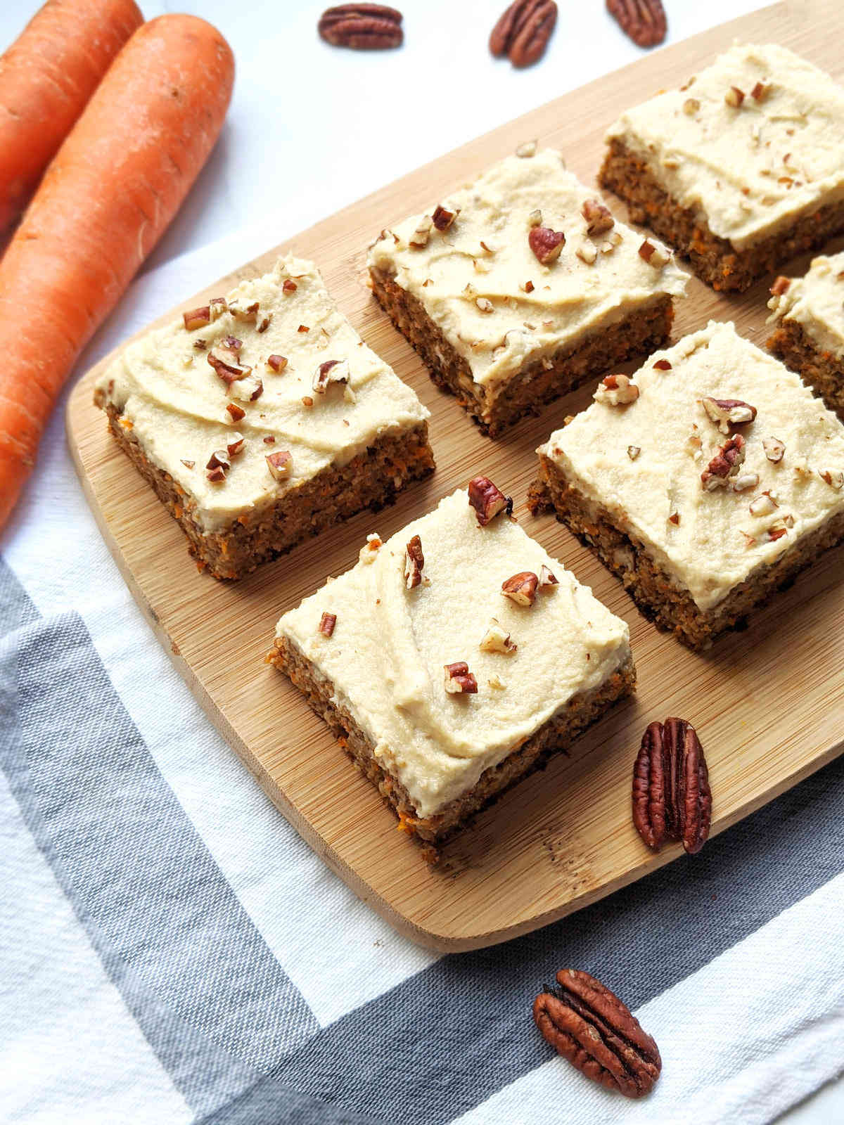 Vegan carrot cake cut into squares with frosting and chopped pecans.