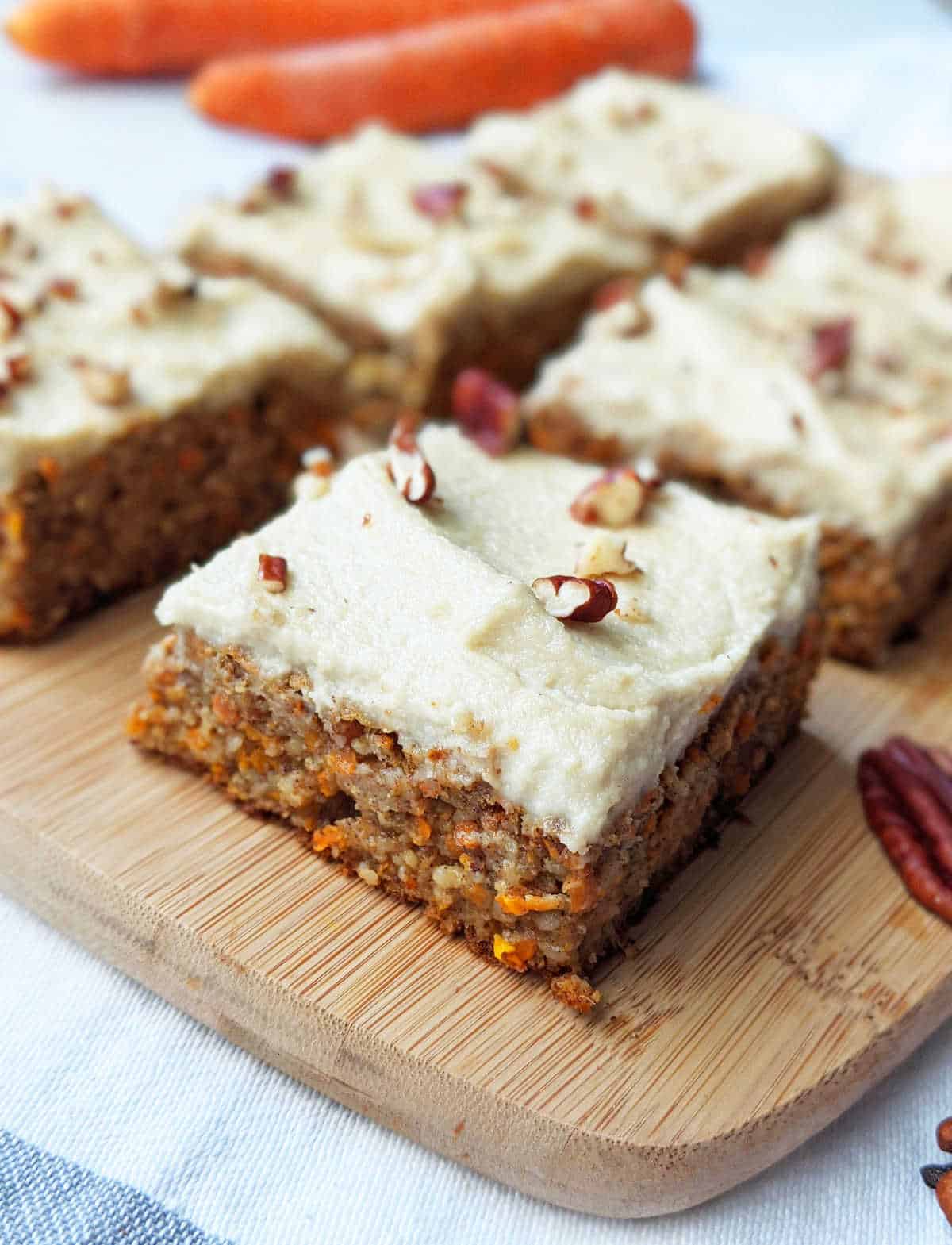 Vegan carrot cake cut into squares with frosting and chopped pecans.