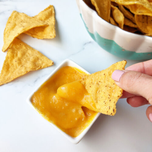 Hand dipping chip into vegan nacho cheese.