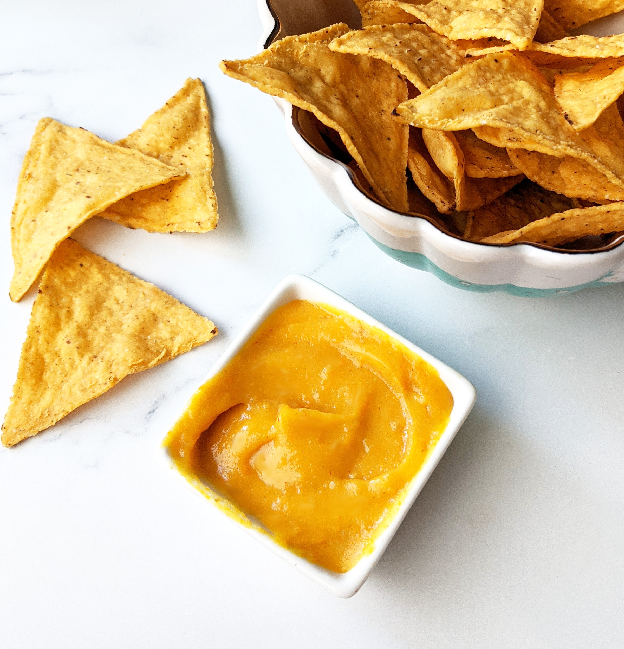 Bowl of tortilla chips next to a small serving bowl of vegan nacho cheese.