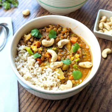 Lentil curry in a bowl with rice and topped with cashews and cilantro leaves.