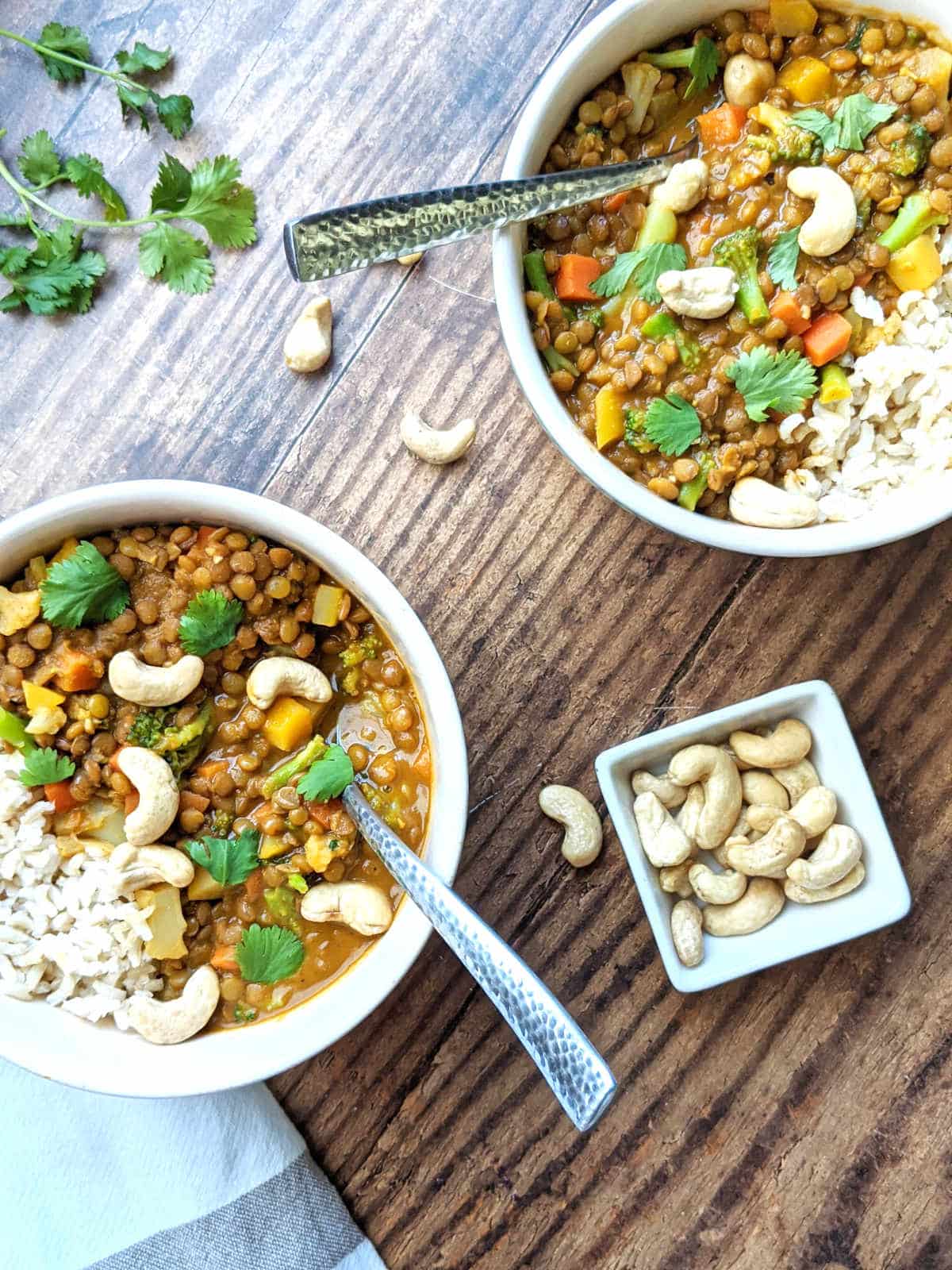 Two bowls of lentil curry with rice on the side and cashews and cilantro on top.