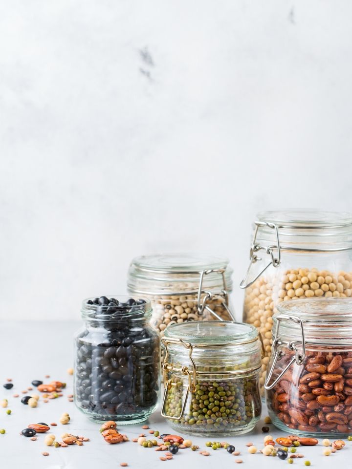 Glass jars full of various vegan proteins including black beans, peas, kidney beans, and chickpeas.