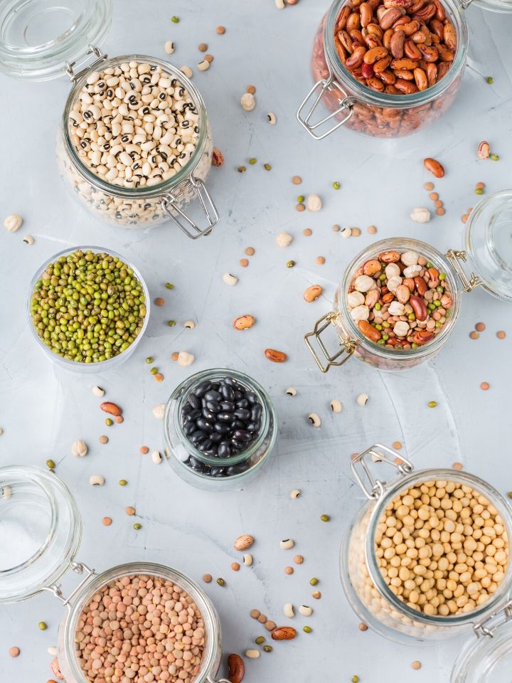 Glass jars full of various vegan proteins including black beans, peas, kidney beans, and chickpeas.