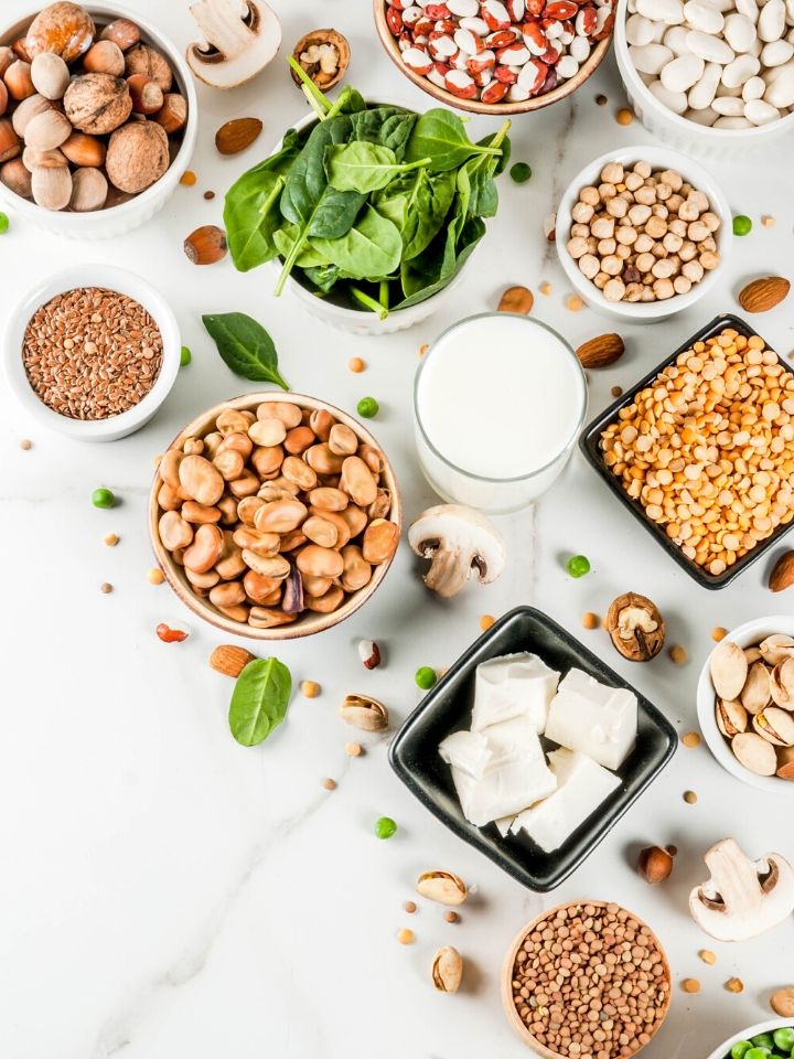 Bowls and ramekins full of different plant proteins including beans, nuts, seeds, tofu, soy milk and leafy greens.