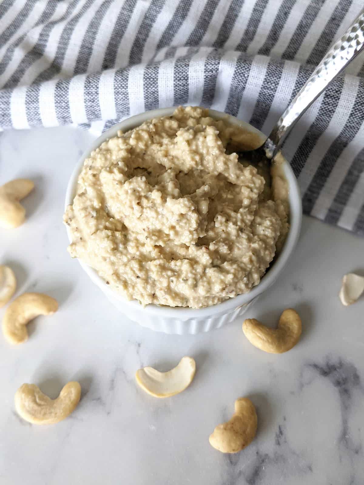 Vegan cashew ricotta in small bowl with spoon and raw cashews next to it.