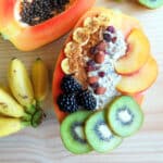 A papaya bowl filled with overnight oatmeal and topped with slices of fresh fruits and nuts.