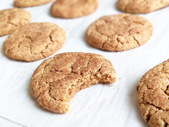 snickerdoodles laying on parchment paper with one cookie with a bite taken out of it