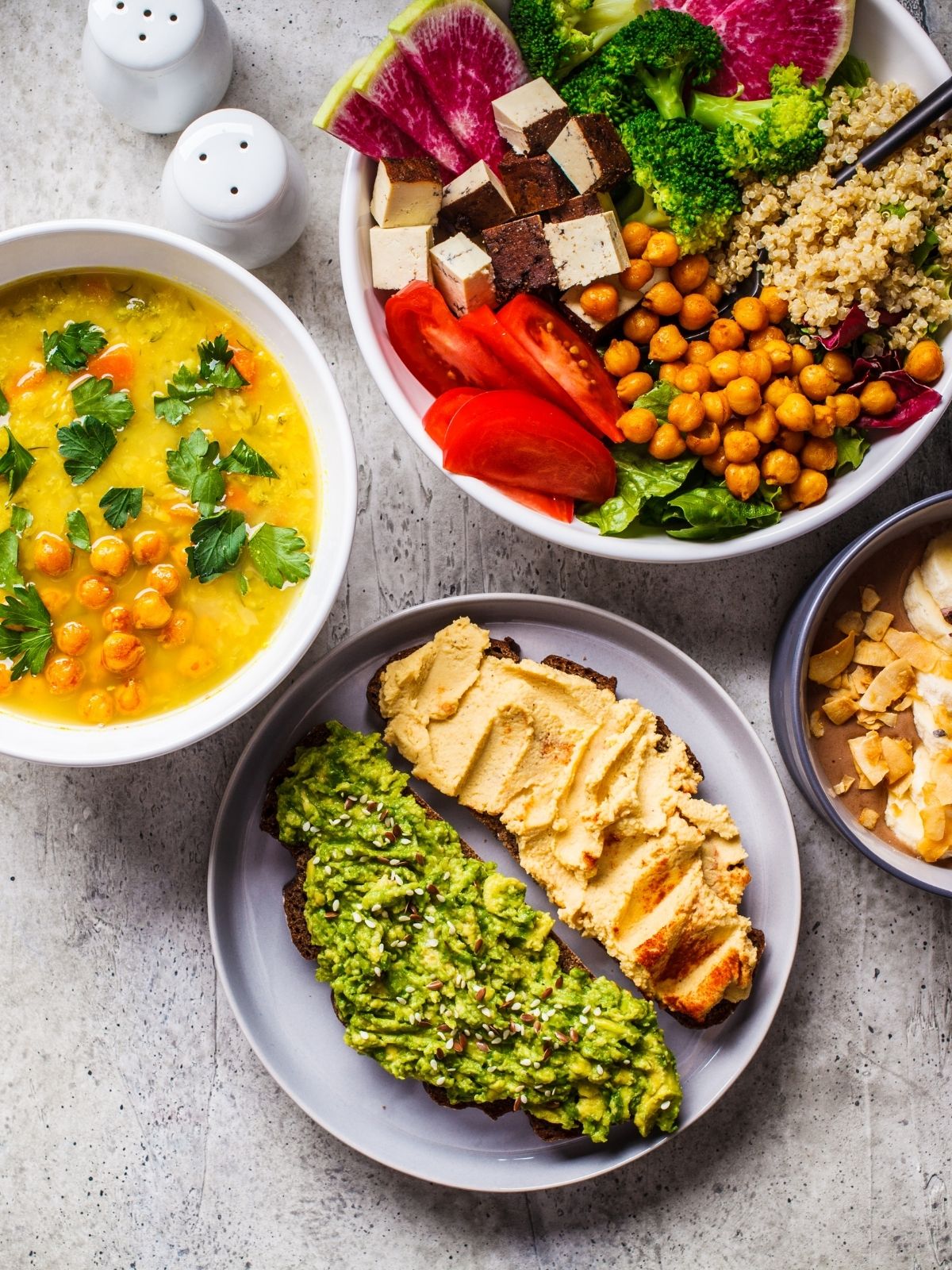 Several bowls of colorful vegan food including soup, toast with different spreads, vegetable and bean bowl, and chocolate nice cream with nuts on top.