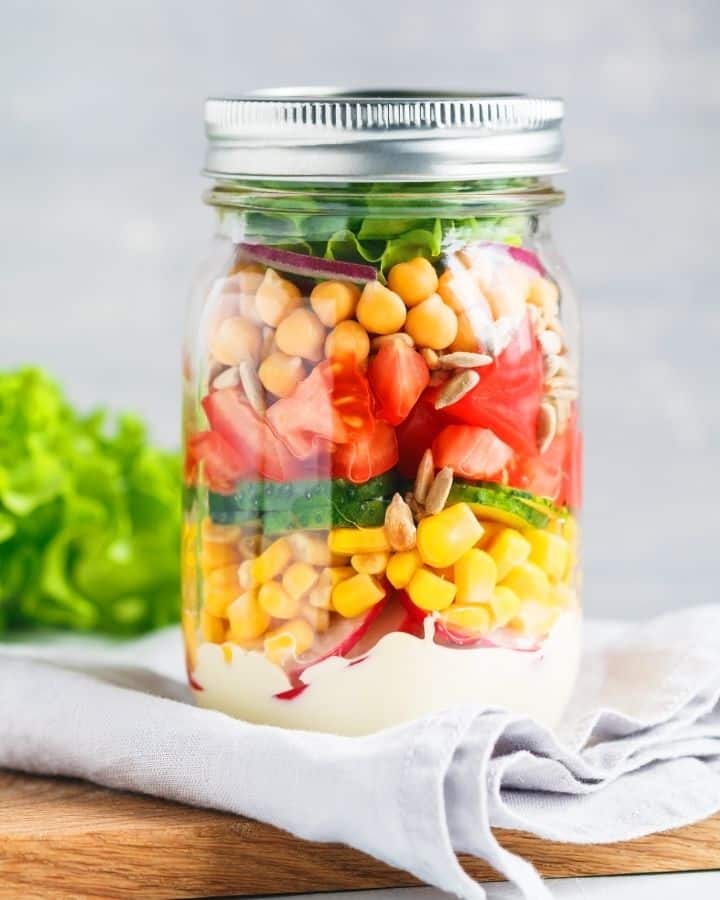 Meal prepped mason jar full of colorful salad ingredients like tomatoes, chickpeas, and corn, with a creamy dressing one the bottom.