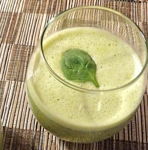 A glass of green tea smoothie topped with a spinach leaf