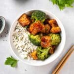 A vegan meal prep bowl with rice, tofu, broccoli, and vegan stir fry sauce.