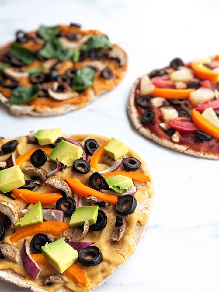 Up close image of three pita pizzas with a variety of toppings and sauces.