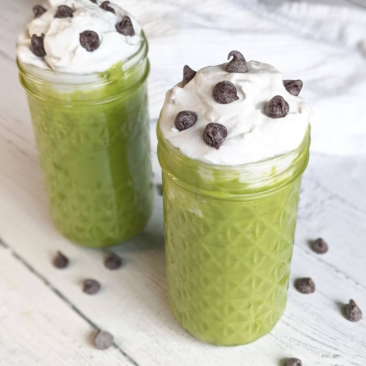 two vegan shamrock shakes topped with coconut whipped cream and vegan chocolate chips