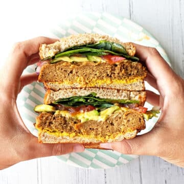 Hands holding two BBQ Seitan Sandwiches over a plate