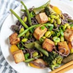 Tofu and vegetable stir fry with black rice noodles on a plate with chopsticks