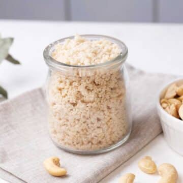 Homemade nutritional yeast substitute in a glass jar next to a bowl of cashews.