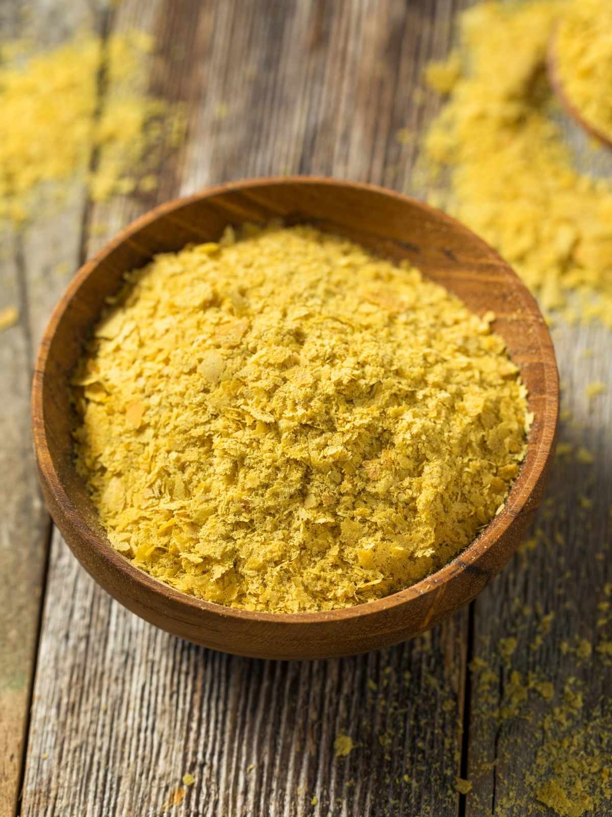 Nutritional yeast in a small bowl on a wooden surface.