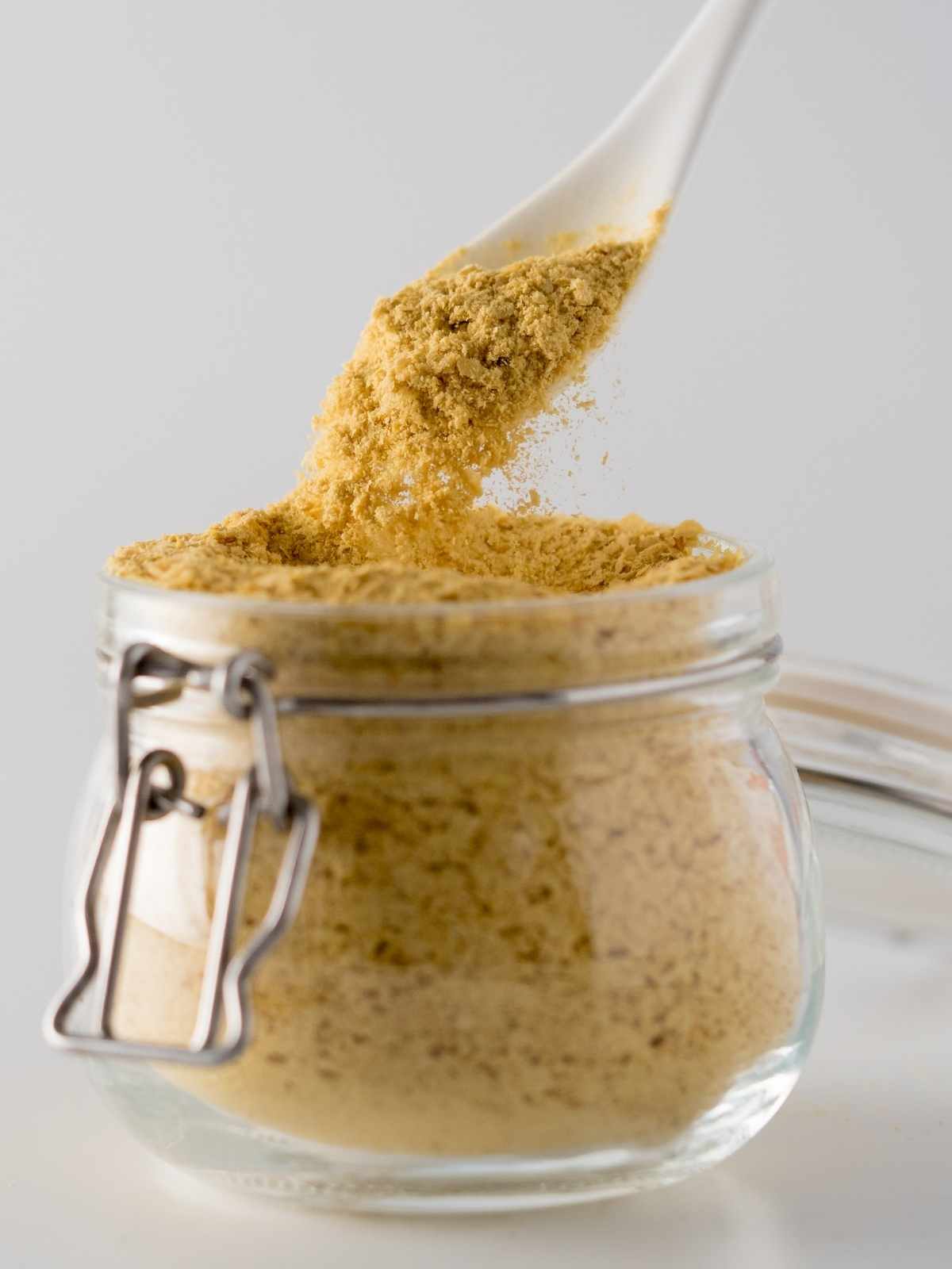 Spoon scooping nutritional yeast out of a glass jar.