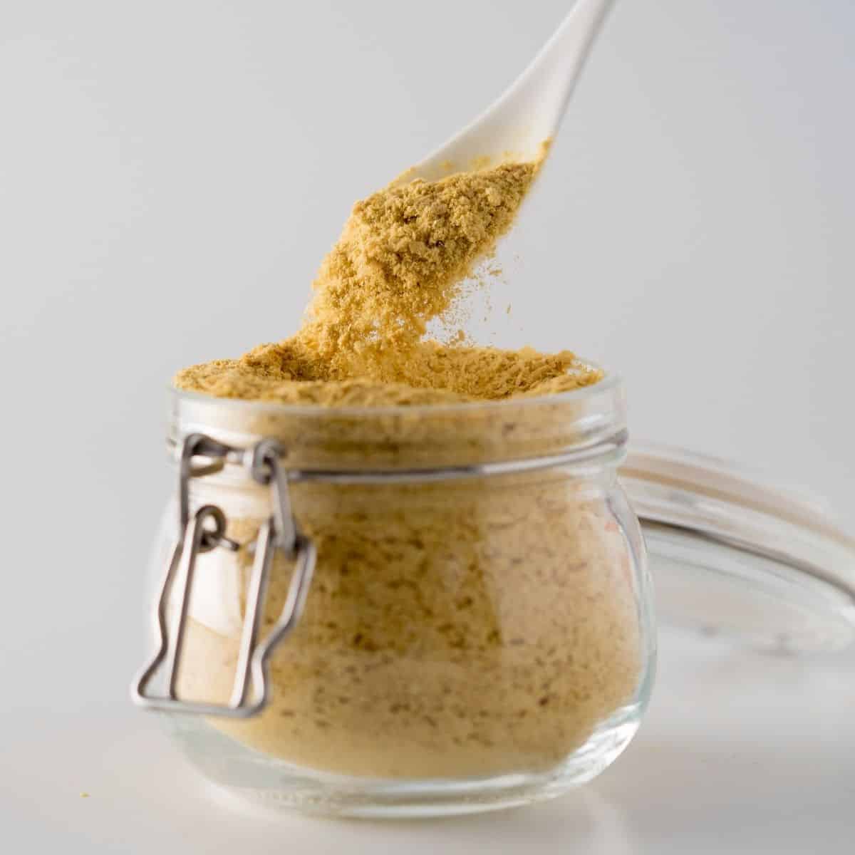 Spoon scooping nutritional yeast out of a glass jar
