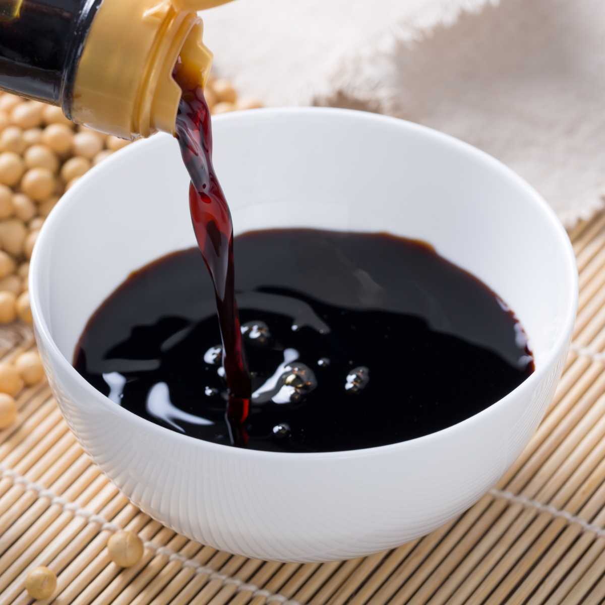 Soy sauce pouring out of a bottle into a bowl.