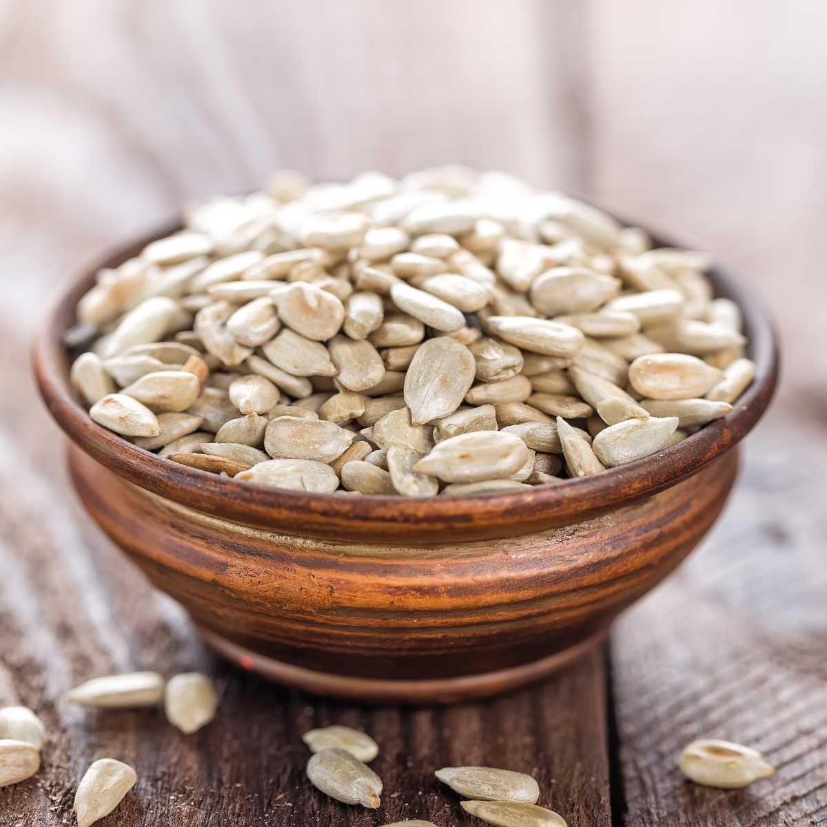 Shelled sunflower seeds in a bowl with some scattered around.