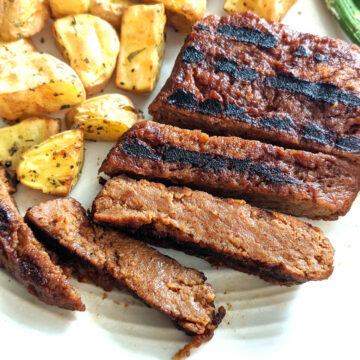 Vegan steak cut into slices on a plate with golden potatoes.