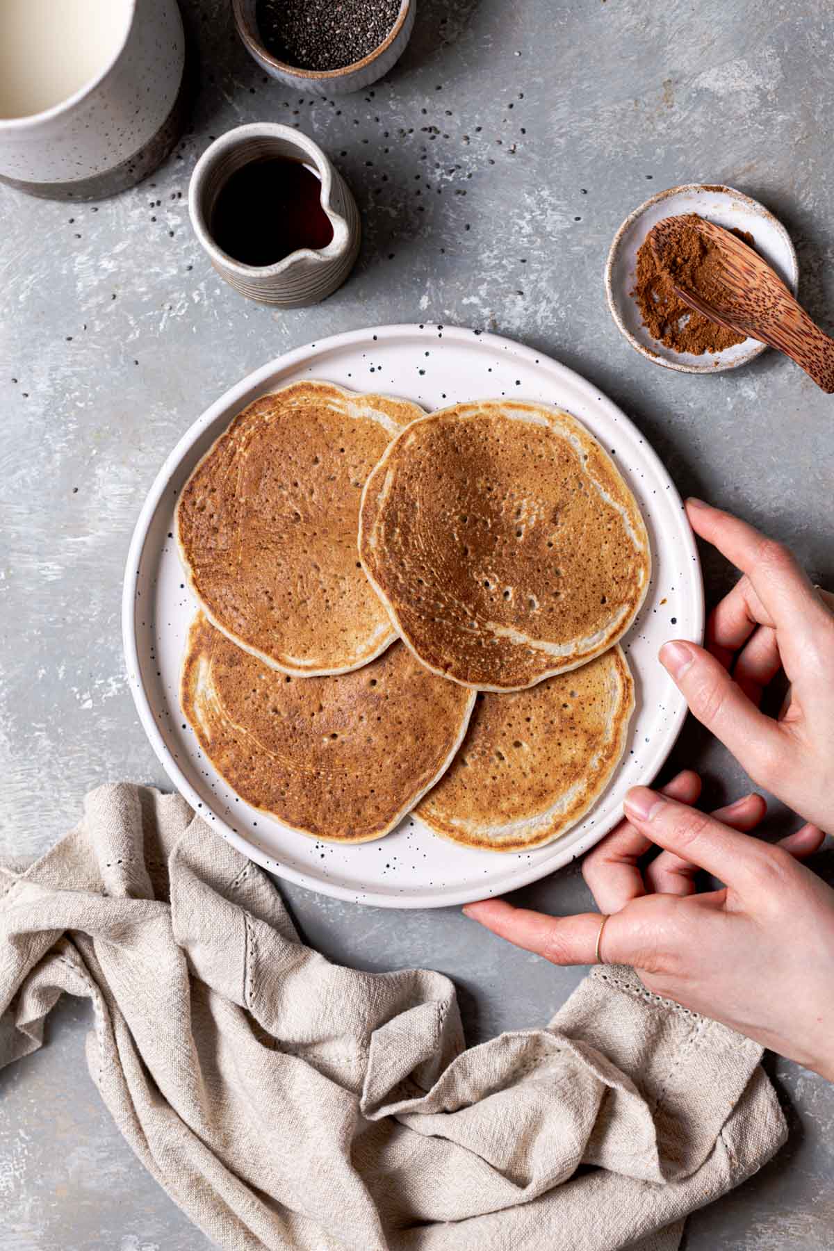 Plate with 4 pancakes on it and hands reaching towards it.