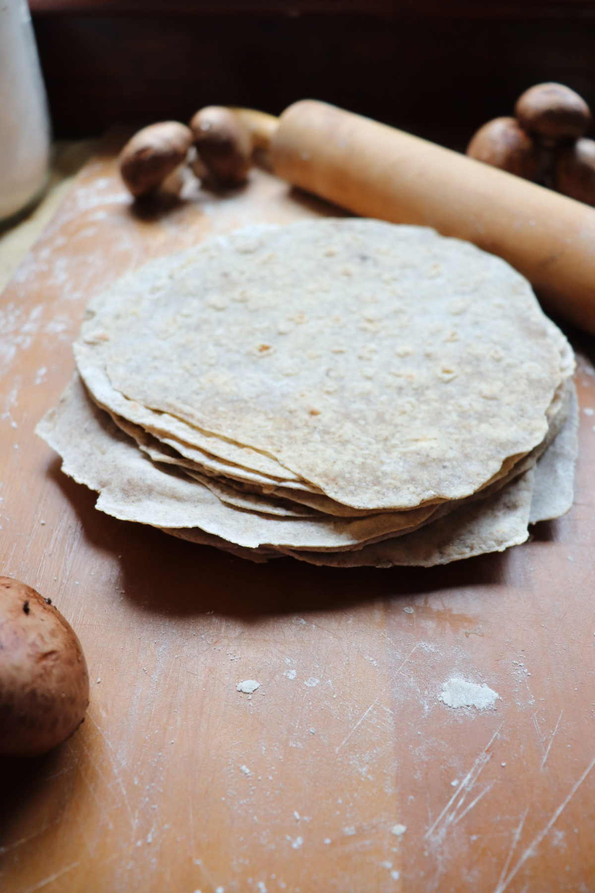 Mushroom tortillas stacked on top of each other next to a rolling pin.