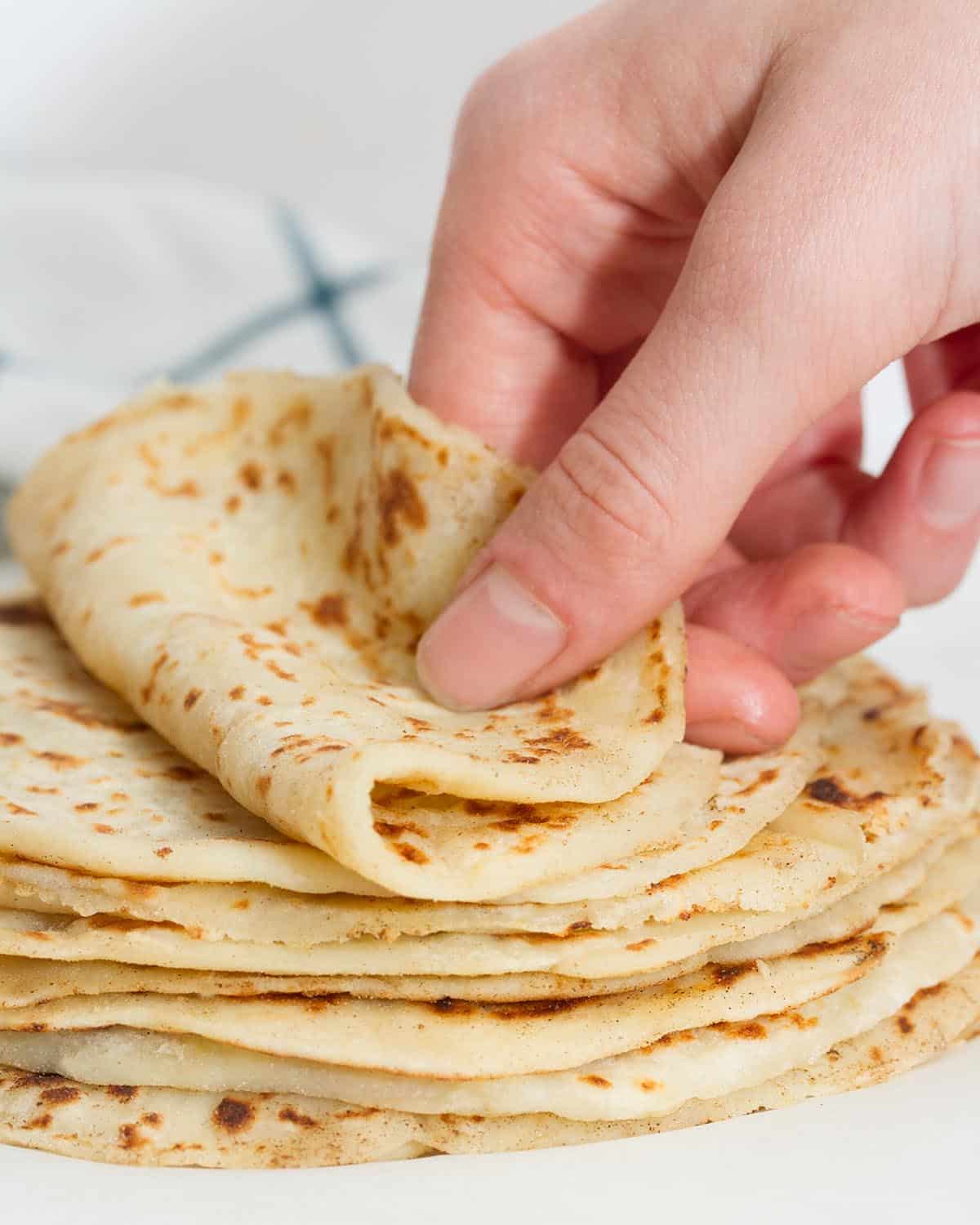 Stack of tortillas with hand folding top tortilla in half.