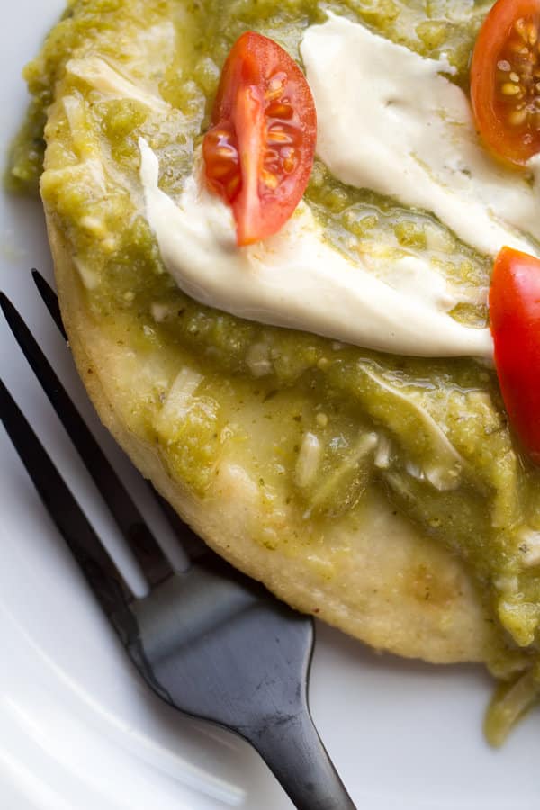 Corn tortilla smothered in green salsa and tomatoes.