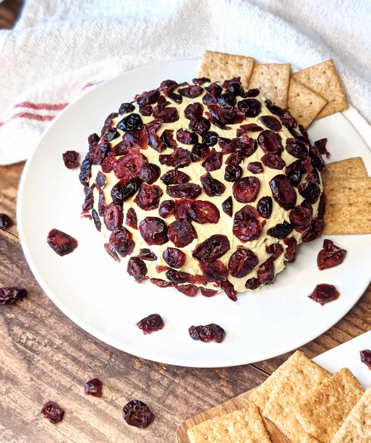 Vegan cheese ball covered with cranberries on a plate with crackers.